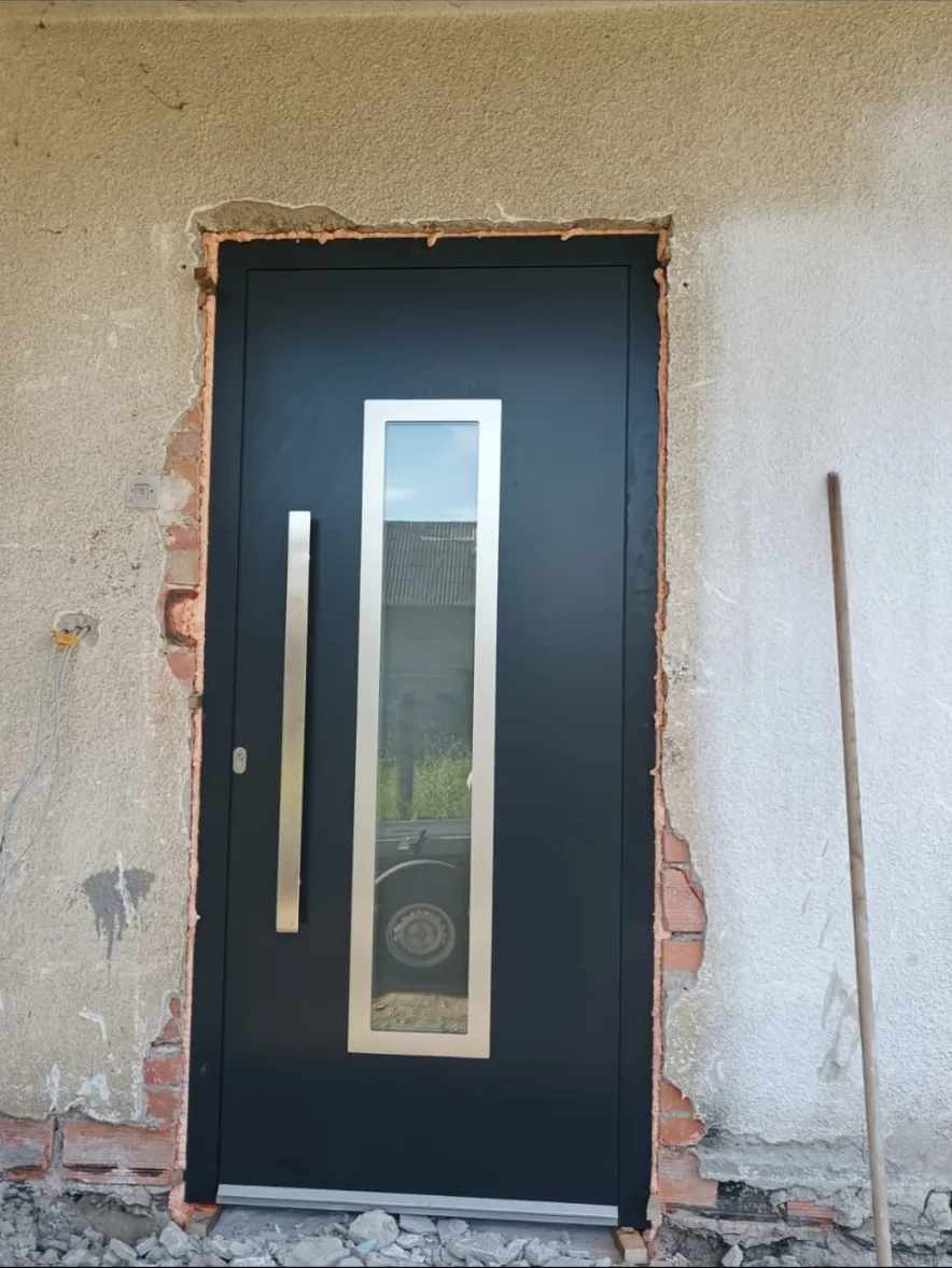 Antracitna aluminijska ulazna vrata s uspravnom ručkom i uskim staklom, ugrađena u obiteljsku kuću